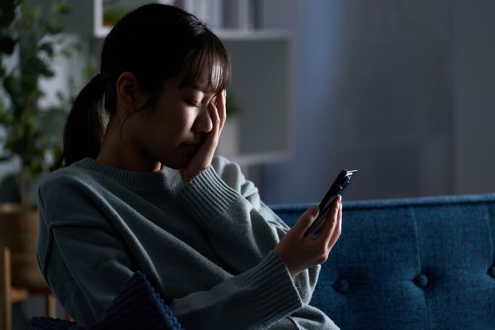 暗い部屋でスマートフォンを見ながら涙をぬぐう女性